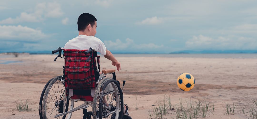 Image of male child in a wheelchair playing with a soccer ball